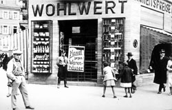 Würzburg, „Tag des Boykotts“, 1. April 1933. Ein SS-Mann steht vor einem jüdischen Kaufhaus. An dem blockierten Eingang  ruft ein Plakat mit den Worten „Kampf gegen Warenhäuser“ zum Boykott des Geschäftes auf