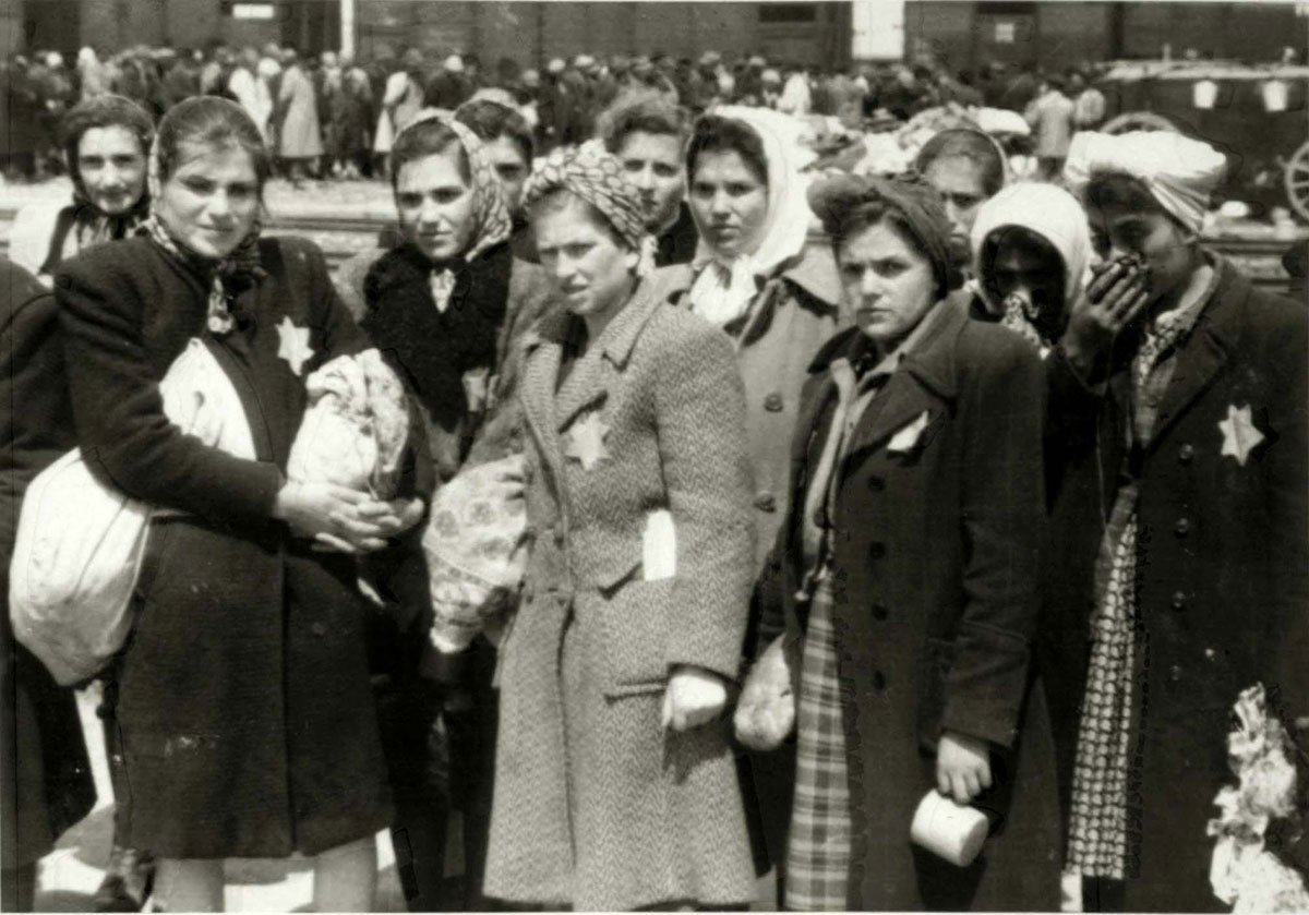 Diese jüdischen Frauen sind nun Häftlinge in Auschwitz. Sie durften kleine Beutel mit ihren Habseligkeiten mitnehmen. Erste Reihe (v.l.n.r.): Lili („Bobo") Yakobovics aus Tacovo (überlebte den Holocaust), Rozi Bittman, Rozi Grever (überlebte den Holocaust). Zweite Reihe: Ester Klein, Sima Müller, Mariska Müller