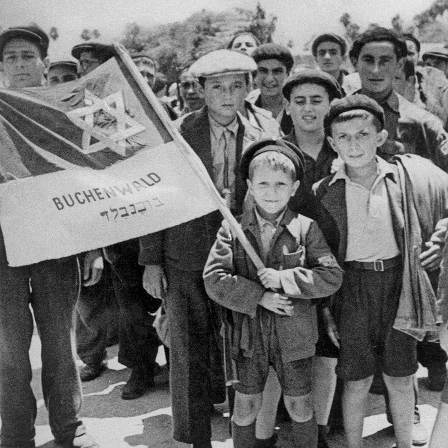 Israel Meir Lau at Haifa Port on the way to Atlit Detention Camp holding a flag with other survivors from Buchenwald. Behind the flag to the left- his brother Naphtali